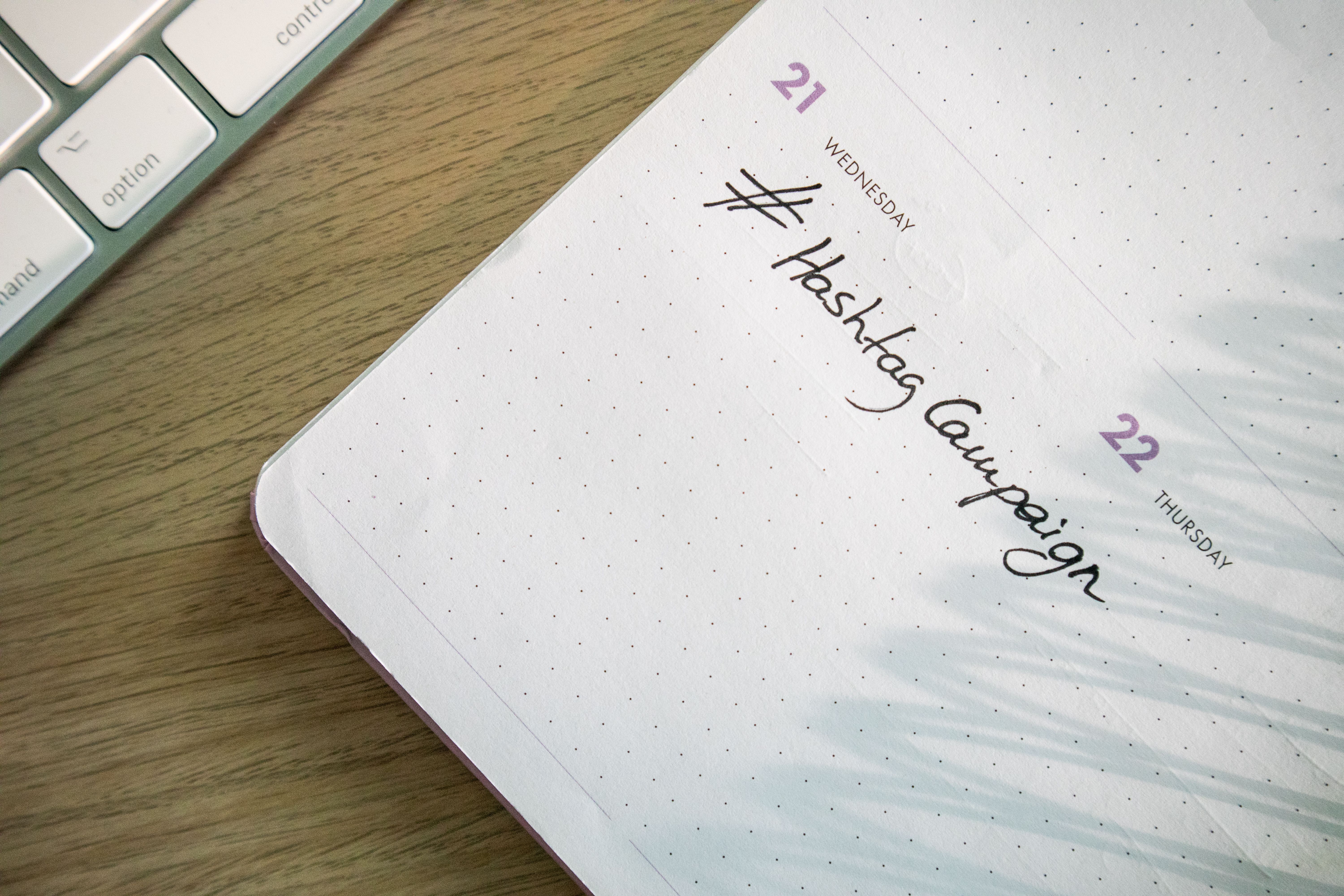 Open planner with a hashtag campaign note beside a computer keyboard